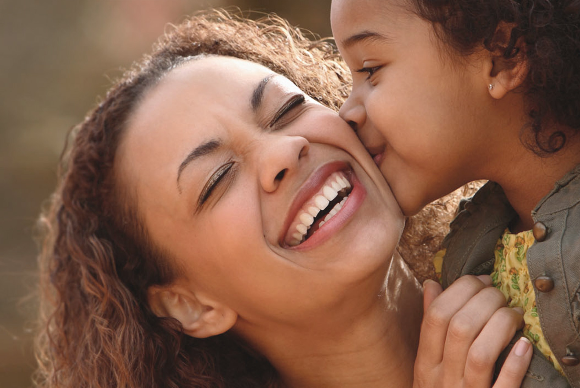 A woman and a child are sharing a joyful moment, with the woman smiling broadly at the camera while holding the child close.