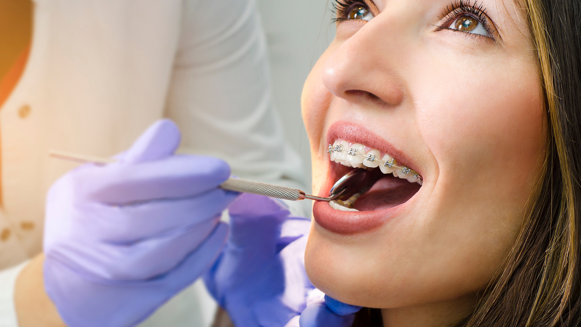 The image shows a person receiving dental care, with a dental professional performing a procedure and the patient wearing a surgical mask.