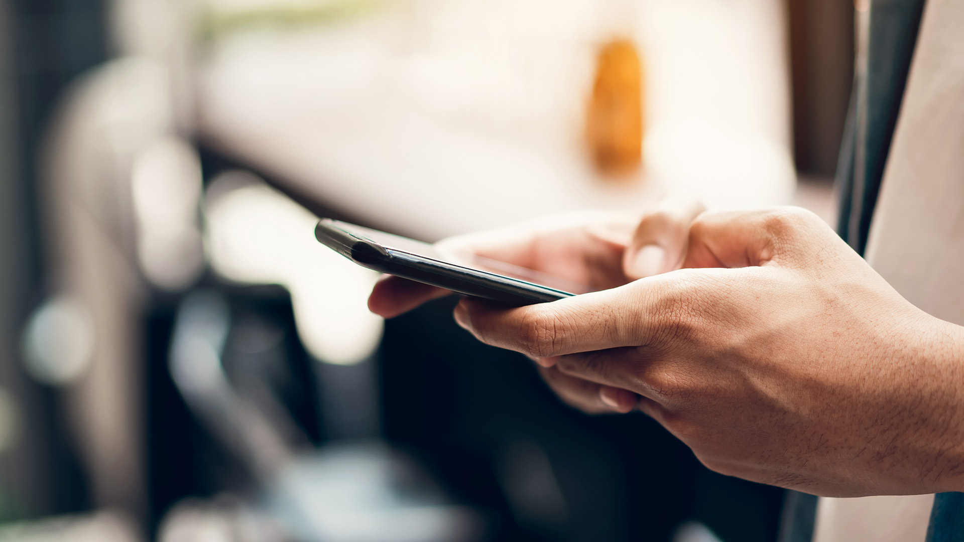 The image shows a person using a smartphone, captured from the back with a focus on the device s screen.