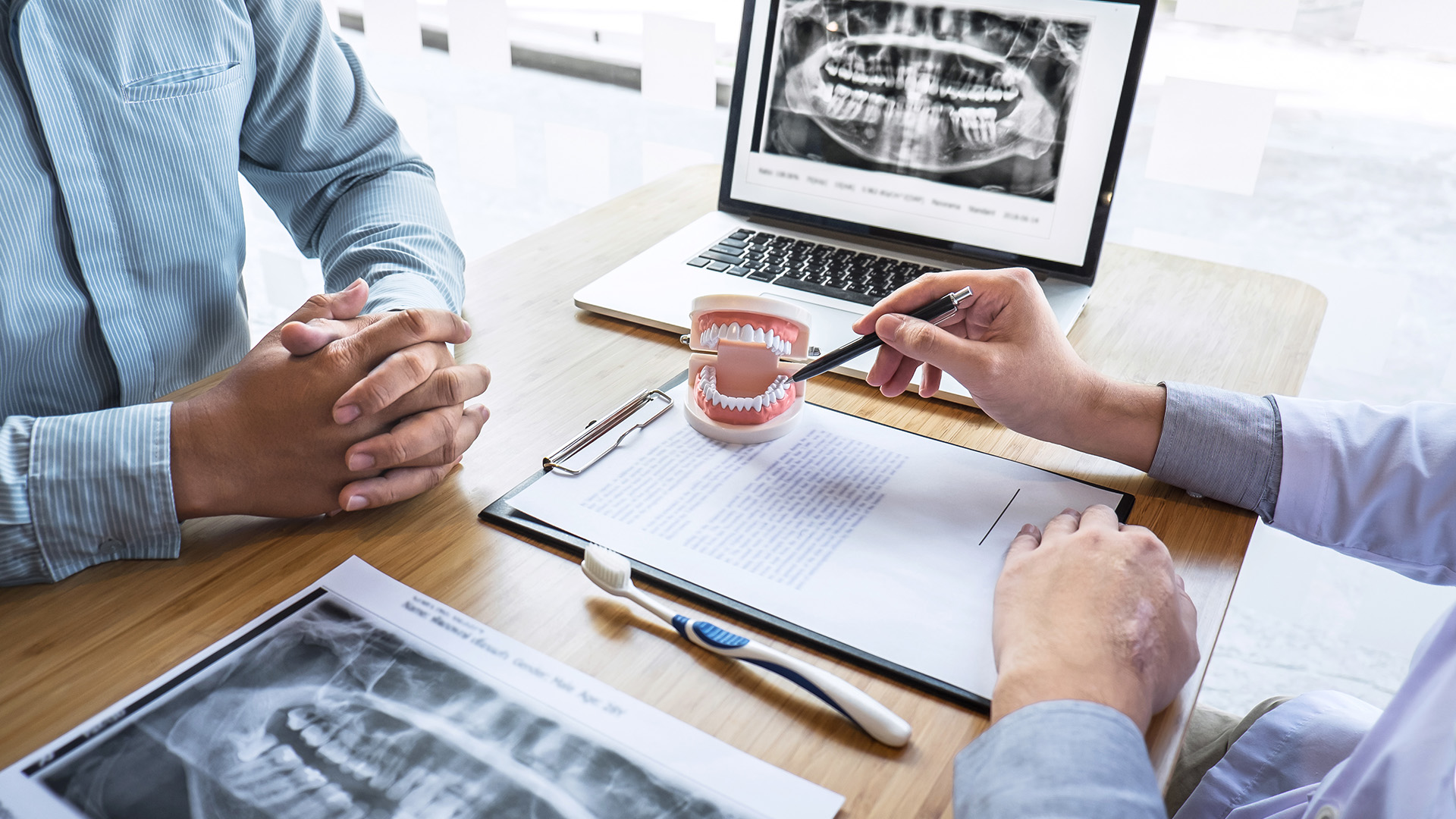 Two professionals in a medical setting, one with a model of a human mouth and teeth, discussing dental care.