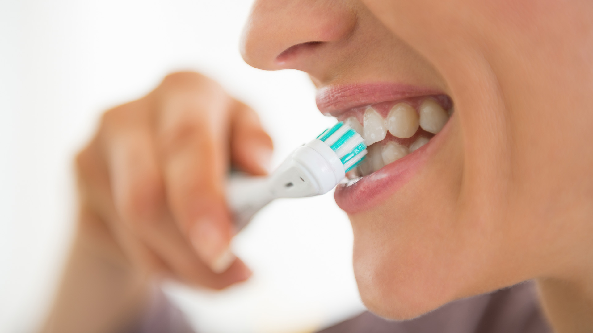 The image shows a person brushing their teeth with an electric toothbrush.