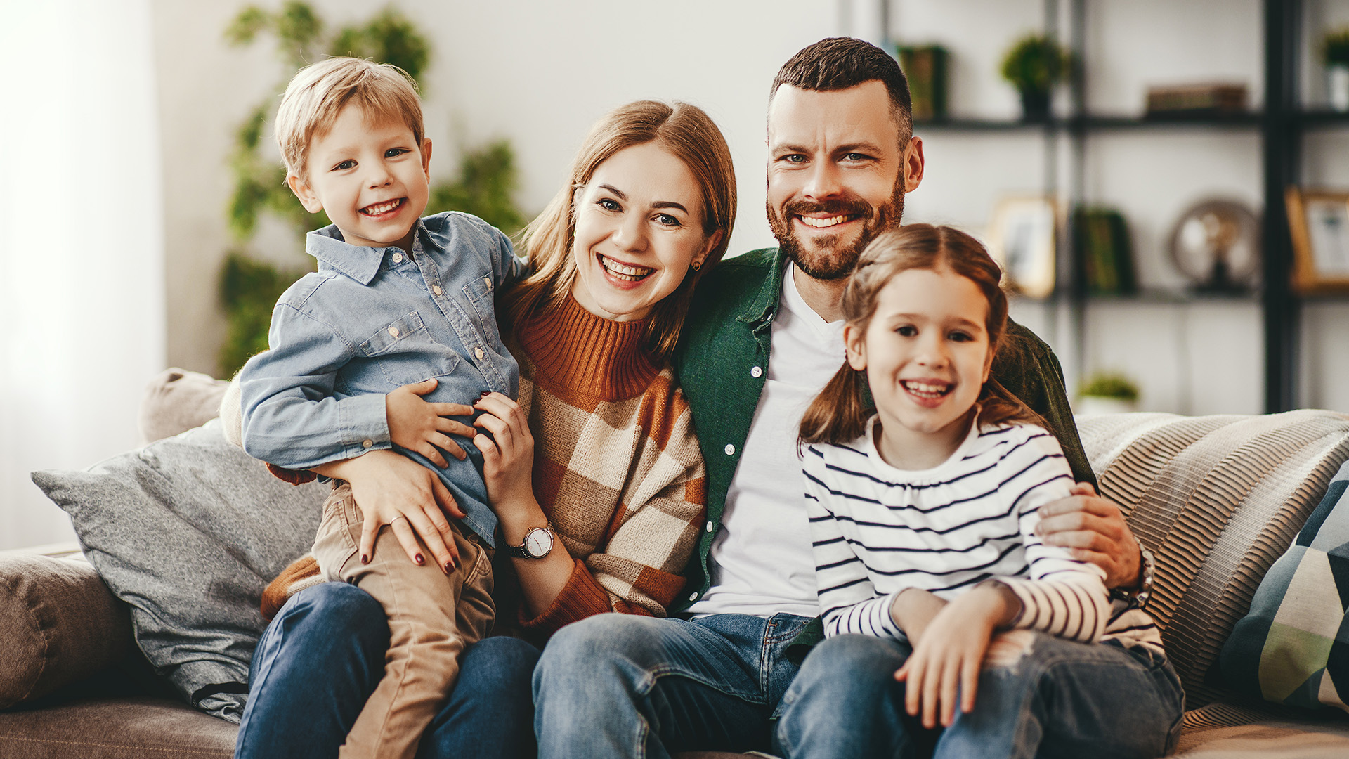 A family of four, with a man, woman, and two children, posing together in a cozy living room setting.