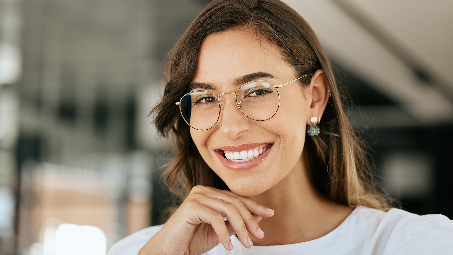 The image shows a smiling woman with glasses, wearing a white top and a necklace, posing for the camera.