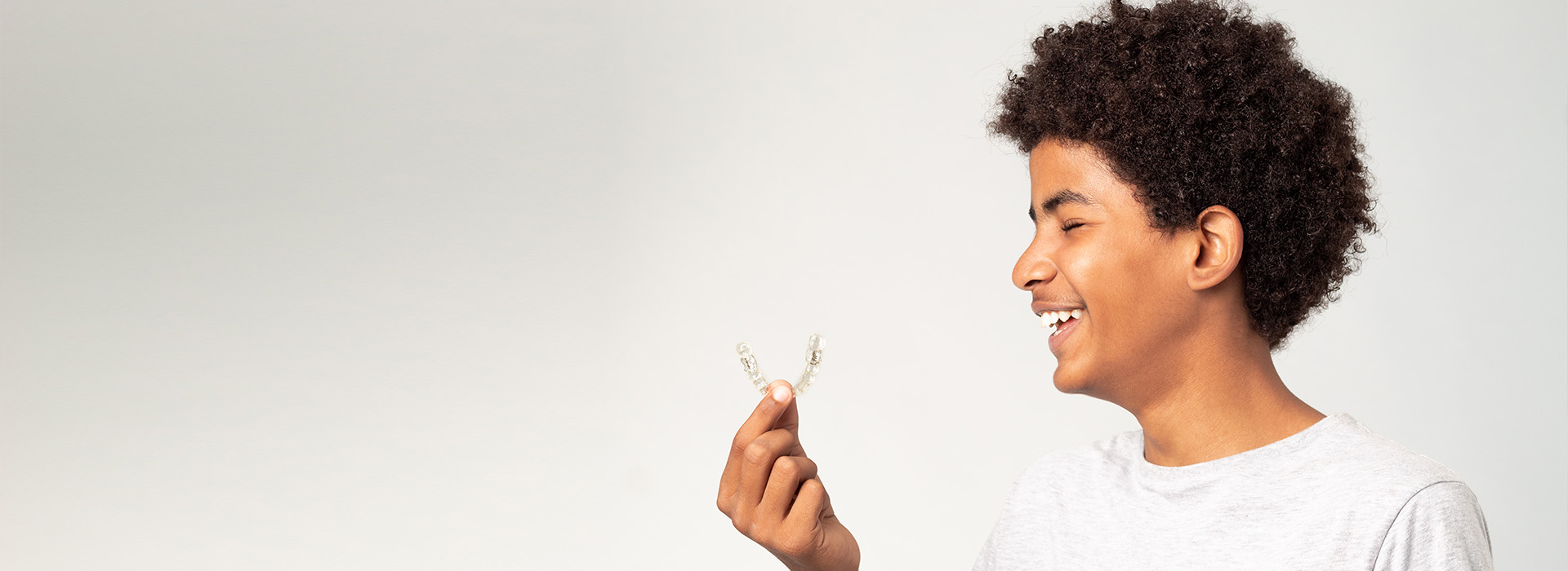 The image shows a young person holding a white feather and smiling, with a blurred background that suggests an indoor setting.