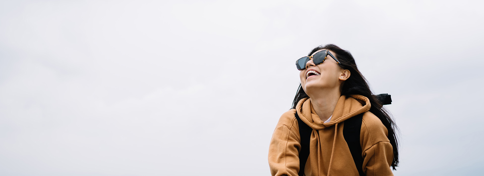 A person in a hoodie with sunglasses, standing outdoors against a sky background.