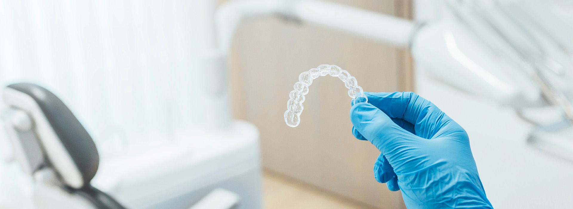 A hand holding a transparent dental impression material, set against the backdrop of a dental office environment.