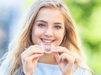 A smiling woman holding a dental retainer with both hands.