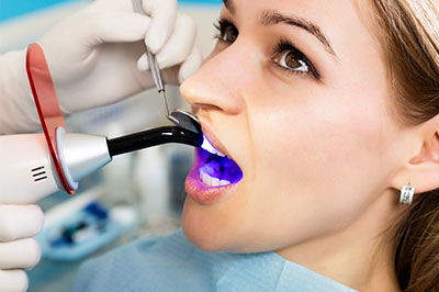 A woman in a medical setting receiving dental care, with a dental device inserted into her mouth and a dental hygienist using an ultrasonic cleaning tool.