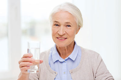 An elderly woman holding a glass of water with a smile.