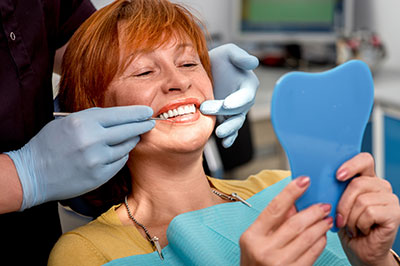 A woman is sitting in a dental chair, receiving dental care with a smile on her face.