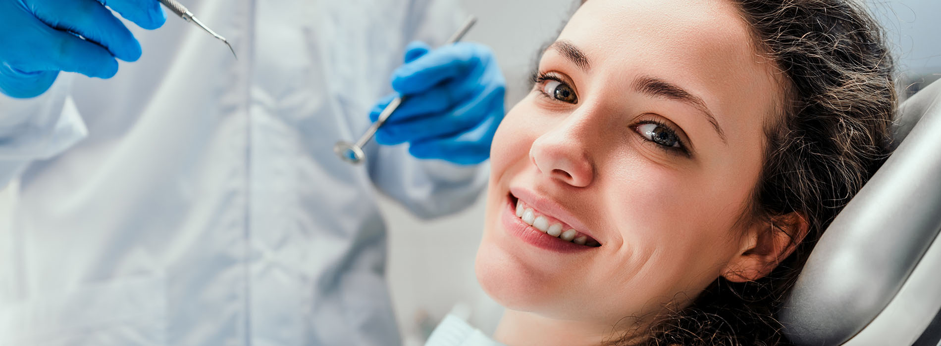 An adult woman receiving dental care with a smiling expression, while dental professionals work in the background.