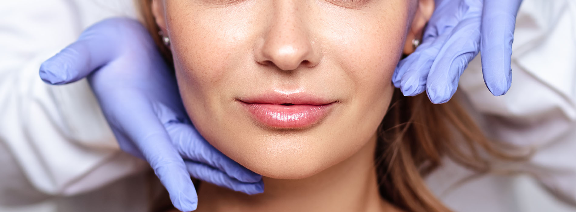 A woman receiving a facial treatment, with a close-up view of her face and the hands of a professional applying a mask or cream.