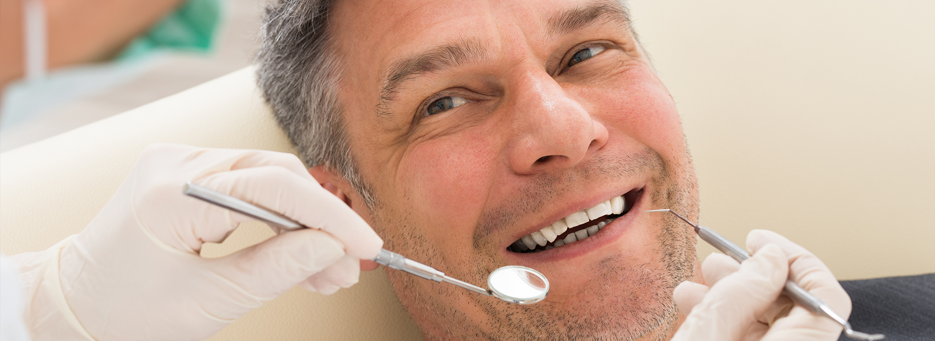 A man in a dental chair receiving dental treatment, with a smiling expression and his mouth open.