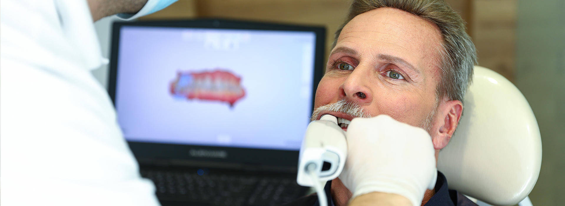 A man receiving dental treatment, with a dental professional using a computer to assist in the procedure.