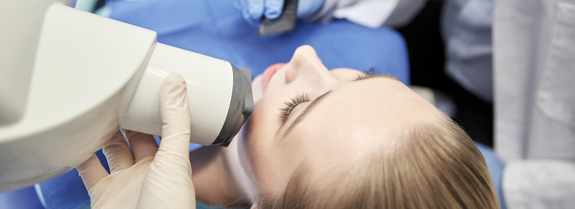 A person receiving a dental implant under the supervision of a dentist, with dental tools and equipment visible.