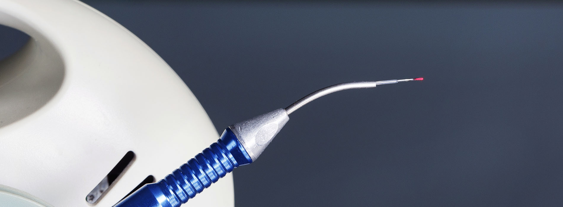 The image shows a close-up of a medical device, possibly a surgical instrument or tool, with a needle-like tip and a blue handle.