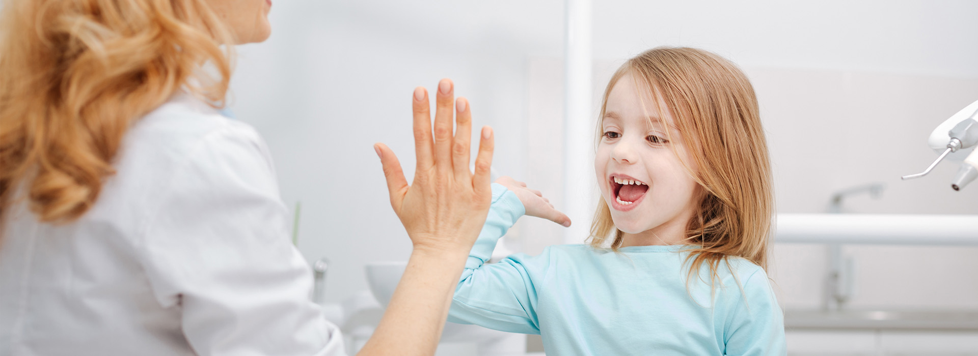 A woman and a young girl in a dental office, with the woman showing something to the child.