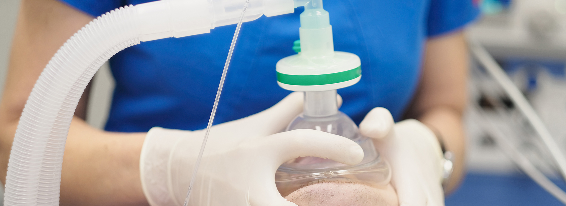 A person in a blue shirt and white gloves is handling a clear medical device with tubes, possibly for medical or scientific purposes.