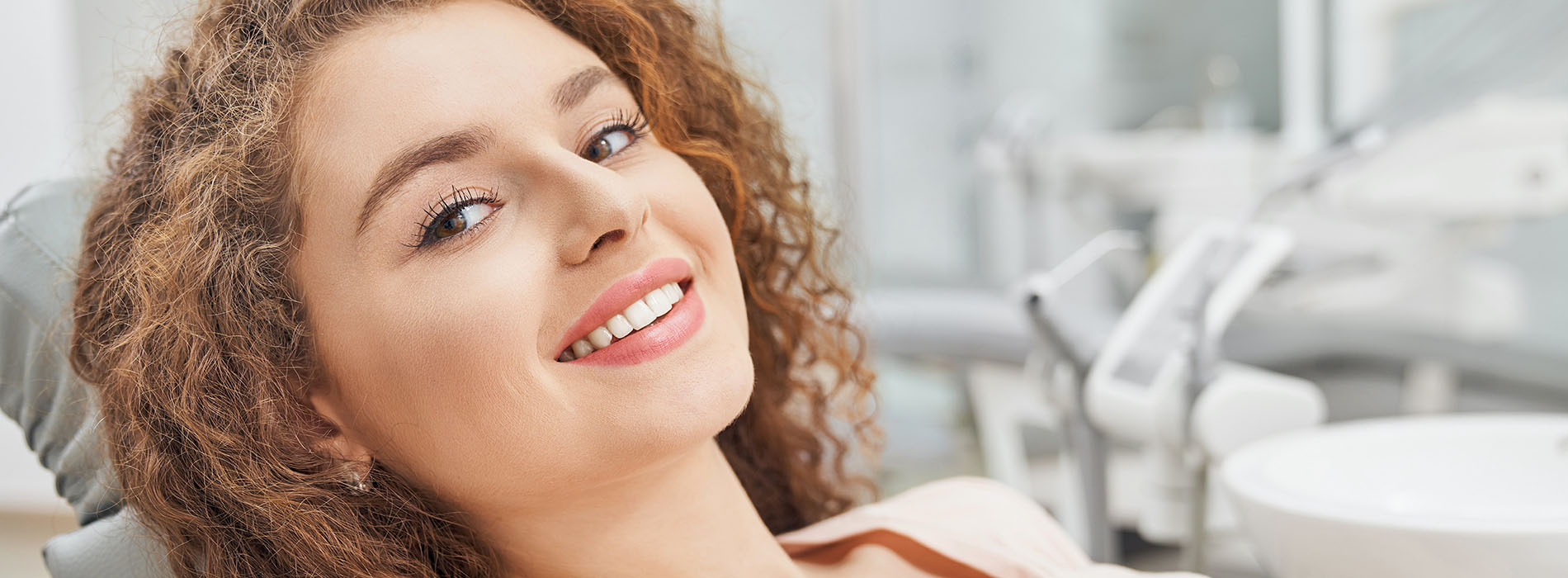 A woman is smiling while sitting in a dental chair, surrounded by dental equipment.