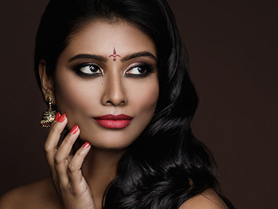 An image of a woman with dark hair, wearing makeup and a red lipstick, posing against a dark background.