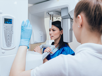 The image features a woman in a blue medical gown, standing next to a large, modern MRI machine, with another person observing the equipment.