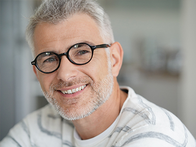 A man with a beard, wearing glasses and a white shirt, is smiling at the camera.