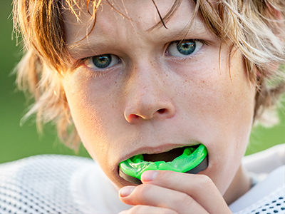 The image shows a young male with blonde hair, wearing a football jersey and holding an object that appears to be a toothbrush in his mouth.