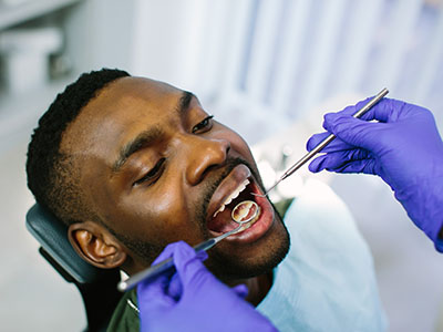 The image depicts a man receiving dental care, with a dentist performing work on his teeth while wearing gloves and using dental instruments.