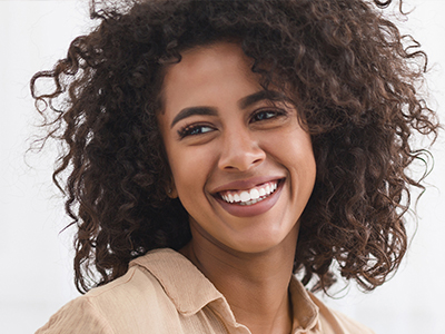 A woman with curly hair is smiling and looking directly at the camera.